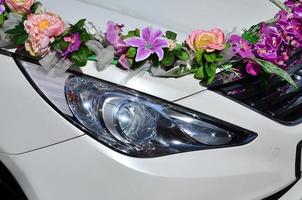 une photo détaillée du capot de la voiture de mariage, décorée de nombreuses fleurs différentes. la voiture est préparée pour une cérémonie de mariage
