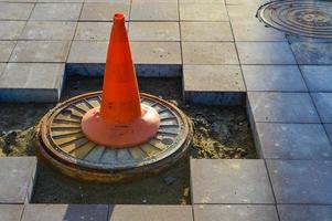 un cône orange vif se dresse sur le drain d'égout. marquage des sections dangereuses sur la route, l'accès aux personnes est interdit. le cône se dresse sur l'asphalte cassé, les constructeurs posent une nouvelle surface