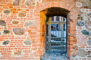 une ancienne porte métallique ancienne avec des barreaux de prison solides sur un épais et large mur de brique fissurée rayée d'argile rouge photo