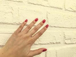 manucure brillante, rouge et brillante sur fond orange mat. mur de briques en plâtre pour les prises de vue des services de beauté des maîtres. mur du salon de beauté. photographie créative des ongles photo