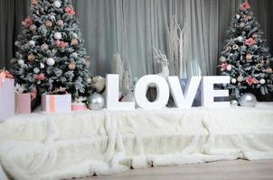 intérieur cosy du nouvel an avec un grand voile en peluche, deux arbres de noël, des animaux de la forêt jouets et l'inscription amour de grandes lettres blanches photo
