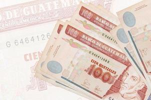 100 billets de quetzales guatémaltèques sont empilés sur fond de gros billets semi-transparents. présentation abstraite de la monnaie nationale photo