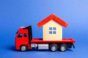 camion rouge transporte une maison au toit rouge. concept de transport et d'expédition de fret, entreprise de déménagement. construction de nouvelles maisons et objets. industrie. logistique et approvisionnement. déplacer des bâtiments entiers. photo