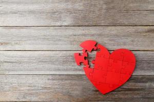 Coeur de puzzle rouge sur fond de bois gris