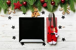 vue de dessus de la fourchette, du couteau et de l'assiette entourés de sapins et de décorations de noël sur fond en bois. concept de réveillon du nouvel an et de dîner de vacances photo