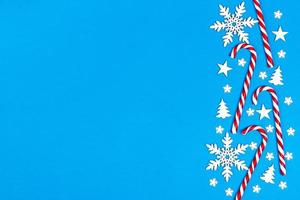 canne en bonbon de noël se trouvait uniformément dans la rangée sur fond bleu avec flocon de neige décoratif et étoile. mise à plat et vue de dessus photo