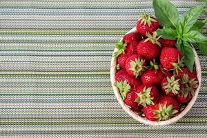 fraises sucrées mûres dans un panier en osier et des feuilles de menthe. photo