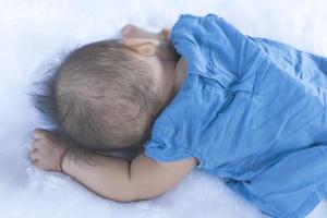 un enfant se couche sur un drap blanc dans une chemise bleue. photo