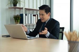 concept d'apprentissage, de réunion, de travail et d'apprentissage en ligne en ligne. homme d'affaires asiatique décontracté étudiant un cours en ligne, se rencontrant via un ordinateur portable au bureau. photo