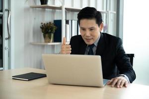 concept d'apprentissage, de réunion, de travail et d'apprentissage en ligne en ligne. homme d'affaires asiatique décontracté étudiant un cours en ligne, se rencontrant via un ordinateur portable au bureau. photo