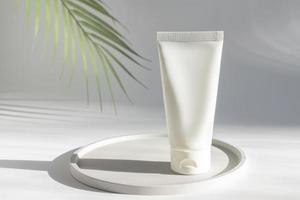 le tube de crème cosmétique se dresse sur un plateau en céramique sous une feuille de palmier verte, une maquette d'emballage de produit de beauté et de soin vierge photo