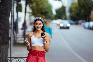 femme dans la rue buvant du café le matin et utilisant un smartphone. photo