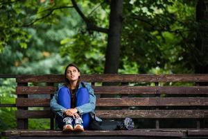 femme pensive assise sur un banc dans un parc regardant loin photo