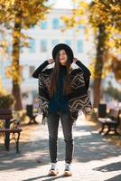 femme élégante en poncho et chapeau profite du parc d'automne photo