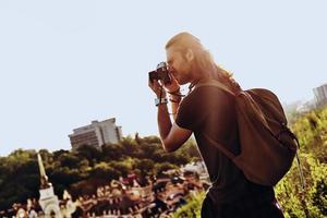 je dois capturer ce jeune homme en tenue décontractée en train de photographier la vue en se tenant debout sur la colline à l'extérieur photo