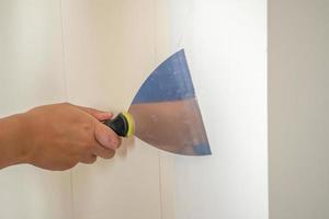 homme réparant un mur blanc fissuré avec une spatule photo
