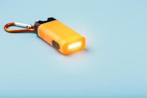une lampe de poche à led orange avec un mousqueton brille sur un fond bleu. photo