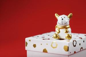 taureau jouet du nouvel an 2021 avec un cadeau sur fond rouge. coffret cadeau et perles dorées. photo