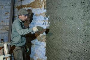 un homme jette du mortier de béton sur le mur, la première couche de plâtre sur le mur, des travaux de réparation en ukraine. photo