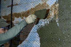 le maître jette une solution de béton liquide sur le mur, la première couche de plâtre sur le mur. photo