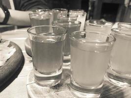 un ensemble de beaucoup de délicieux verres noirs et blancs, des shots avec de l'alcool fort, de la vodka, du remplissage, du brandy sur des supports en bois sur une table dans un café, un bar, un restaurant photo