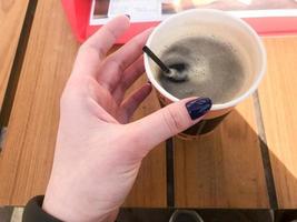 une femme tient avec une belle manucure sur ses doigts un tube dans une tasse de café naturel fort et chaud noir rapide de la restauration rapide dans un verre en papier photo