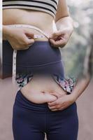 belle grosse femme avec ruban à mesurer, elle utilise sa main pour presser l'excès de graisse isolé sur fond blanc. elle veut perdre du poids, le concept de chirurgie et décomposer les graisses sous le photo