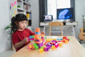 petite fille asiatique mignonne et amusante d'âge préscolaire dans une chemise colorée jouant avec des blocs de jouets lego ou de construction construisant une tour dans la salle de la maternelle ou le salon. les enfants jouent. enfants à la garderie. photo