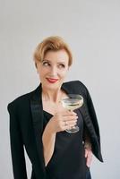 femme élégante et élégante mature en smoking avec un verre de vin mousseux. fête, célébration, concept anti-âge photo