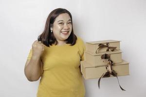 une jeune femme asiatique de grande taille heureuse porte une chemise jaune et tient une boîte de cadeaux et un sac à provisions. photo