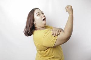 femme asiatique de grande taille excitée portant un t-shirt jaune montrant un geste fort en levant les bras et les muscles en souriant fièrement photo