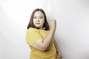 femme asiatique de grande taille excitée portant un t-shirt jaune montrant un geste fort en levant les bras et les muscles en souriant fièrement photo