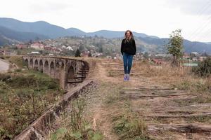 une jeune fille touristique parcourt les anciennes voies ferrées sur le viaduc. ancien viaduc ferroviaire dans le village de montagne de vorokhta. ukraine, carpates. photo