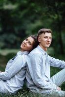 photo en plein air d'un jeune couple heureux amoureux assis sur l'herbe sur la nature. homme et femme étreignant, lumière du soleil dans le parc d'été. famille heureuse dans la lumière du soleil du soir. le concept de vacances.