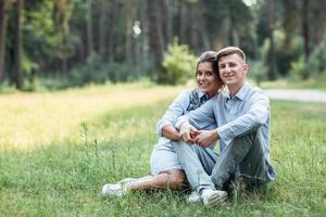 photo en plein air d'un jeune couple heureux amoureux assis sur l'herbe sur la nature. homme et femme étreignant, lumière du soleil dans le parc d'été. famille heureuse dans la lumière du soleil du soir. le concept de vacances