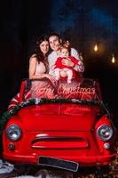 maman, papa et petite fille s'amusant dans la voiture rouge rétro de noël. parents avec une petite fille lors d'une séance photo de noël. tournage en studio avant les vacances.