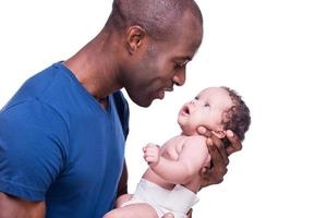 c'est mon garçon vue de côté d'un jeune homme africain heureux tenant son petit bébé et le regardant tout en se tenant isolé sur blanc photo