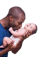 mon bébé jeune homme africain tenant son petit bébé et l'embrassant en se tenant debout isolé sur blanc photo