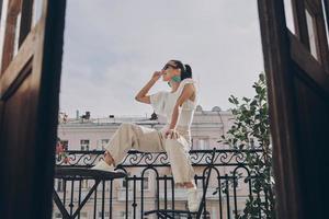 élégante jeune femme ajustant ses lunettes assise sur le balcon photo