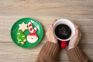 joyeux noël avec une main de femme tenant une tasse de café et un biscuit fait maison sur la table. concept de veille de noël, fête, vacances et bonne année photo