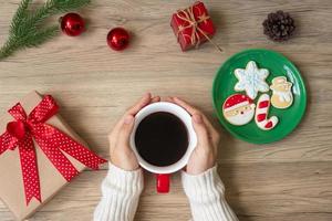 joyeux noël avec une main de femme tenant une tasse de café et un biscuit fait maison sur la table. concept de veille de noël, fête, vacances et bonne année photo