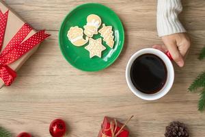joyeux noël avec une main de femme tenant une tasse de café et un biscuit fait maison sur la table. concept de veille de noël, fête, vacances et bonne année photo