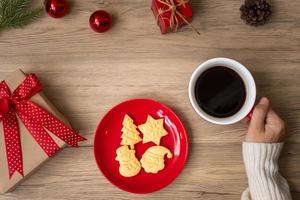 joyeux noël avec une main de femme tenant une tasse de café et un biscuit fait maison sur la table. concept de veille de noël, fête, vacances et bonne année photo