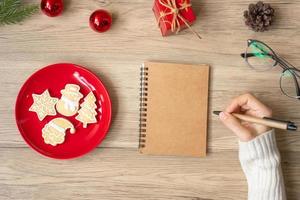 main de femme écrivant sur un ordinateur portable avec des biscuits de noël sur la table. noël, bonne année, objectifs, résolution, liste de choses à faire, stratégie et concept de plan photo