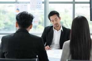 un groupe de jeunes entrepreneurs asiatiques. la haute direction se réunit pour examiner les données d'investissement en actions de l'équipe dans une salle de réunion à la lumière naturelle photo