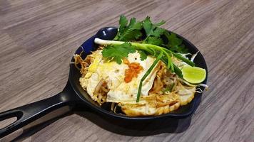 nouilles frites à la thaïlandaise avec crevettes et légumes dans une poêle chaude sur fond bois ou table au restaurant. les asiatiques appellent cette nourriture pad thai et célèbre en thaïlande. repas délicieux photo