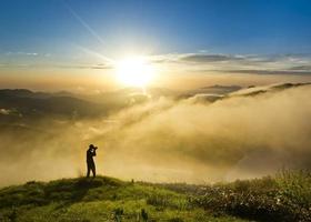 homme sur une colline au coucher du soleil avec caméra faisant photo