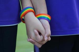 couple de jeunes asiatiques lgbt portant des bracelets arc-en-ciel tenus ensemble pour montrer leur amour. fierté d'être lgbt. mise au point douce et sélective. photo