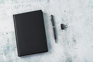 bureau avec bloc-notes noir et stylo sur fond gris. photo