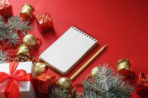 bloc-notes et crayon pour écrire des souhaits et des cadeaux pour le nouvel an et noël autour des décorations d'arbre de noël sur fond rouge. photo